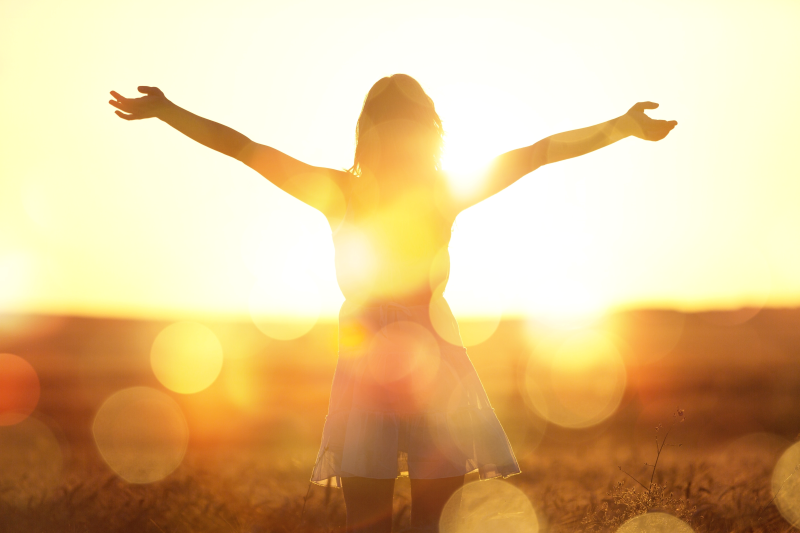 Back of woman looking into sunset arm out