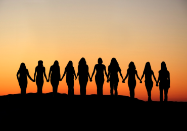Women holding hands facing the sunset